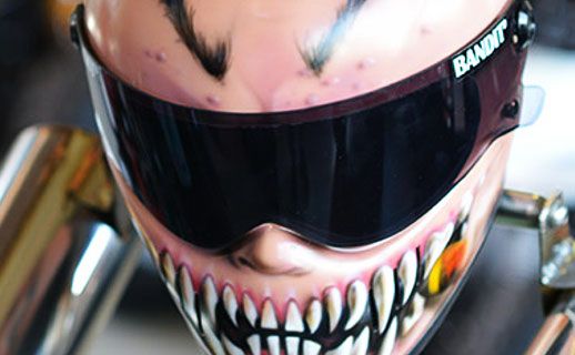 Ein rosa lackierter Motorradhelm mit aufgemalten spitzen Fangzähnen.